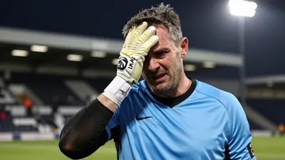 A 35-year-old Dundee goalkeeper with a rugged build and a mix of grey and brown hair, wearing a plain sky blue and black...