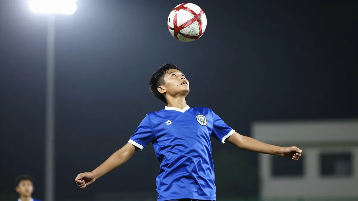 12-year-old midfielder, build lean, wearing East Bengal's blue kit, scoring a powerful header into the top corner, eyes...