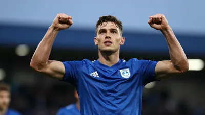 A young, muscular midfielder in a solid blue Derby County kit, celebrating a goal with arms raised