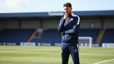 A 30-year-old, tall, athletic-looking Derby County coach, wearing a navy blue tracksuit with a white stripe, stands in...