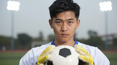 A 28-year-old goalkeeper in a white jersey with a blue collar, holding a football