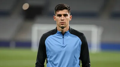 Tall, muscular centre-back in his mid-20s, short dark hair, intense gaze, slight stubble, wearing a plain sky-blue and...