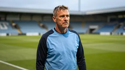 A medium shot of a rugged, 45-year-old Dundee assistant coach, dressed in a plain, unmarked sky blue and black polyester...