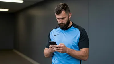 A 35-year-old, 5'10" male assistant coach, with a rugged build and a thick beard, stands in the Pride Park Stadium...