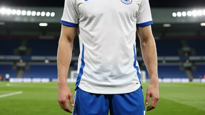 A tight crop of an anonymous Derby County player in a floodlit stadium, wearing a white jersey with a blue stripe, and...