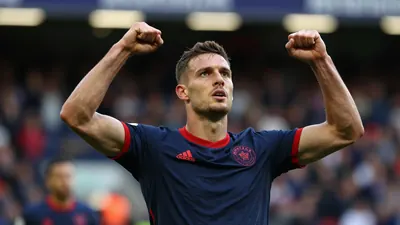 Derby County winger in navy blue jersey with red trim, mid-celebration after scoring, arms raised, sweat visible, intense...