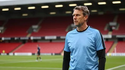 A 35-year-old, 5'10" male football coach with a weathered complexion, wearing a plain, sky blue and black cotton training...