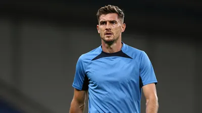 Mid-30s male Derby County coach, athletic build, waist-up, wearing a plain sky-blue and black training top (smooth...