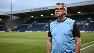 A 50-year-old Derby County assistant coach, with a rugged build and graying temples, stands on the Pride Park Stadium...