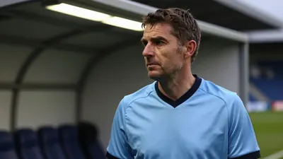 A close-up shot of a 45-year-old male head coach in a plain unmarked sky blue and black polyester home kit, his face set...