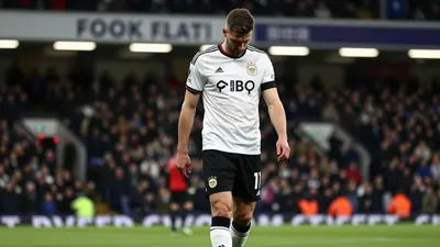 A muscular Derby County midfielder in a white shirt and black shorts, head down in frustration, walking off the pitch...